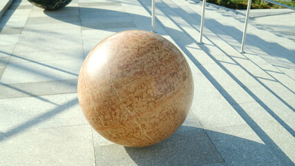 Beige marble sphere on concrete stairs with strong angular shadows