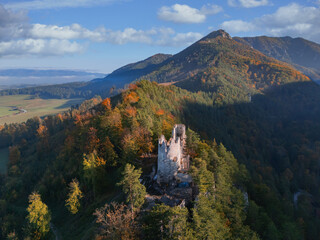 Aerial view of the ancient Blatnica castle ruins amidst the vibrant autumn foliage, with mountains rising in the distance, Blatnica, Zilinsky kraj, Slovakia.