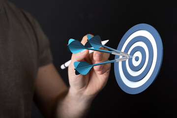 Close-up of hand throwing darts hitting bullseye on dart board. Concept for business success, goal...