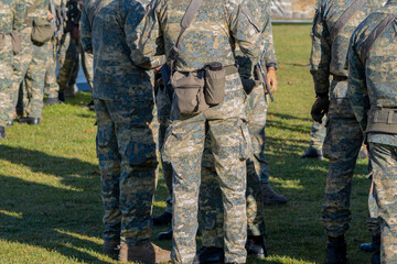 Several soldiers in camouflage uniforms are standing in a group on a grassy field