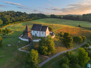 Aerial view of the Church of St. Martin proudly stands atop a gentle hill, bathed in the warm glow of the setting sun, Cerin, Banska Bystrica Region, Slovakia.