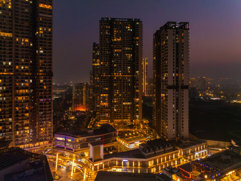 Aerial view of city lights shimmer on modern buildings, juxtaposing the dark sky with the illuminated architecture of Gurugram, Haryana, India.