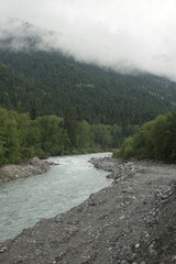 A stormy mountain river flows between rocks, boulders and cliffs in Arkhyz against a backdrop of...