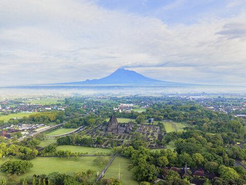 Aerial view of ancient temples stand majestically amidst lush greenery, with Mount Merapi looming softly in the distance, Yogyakarta, Daerah Istimewa Yogyakarta, Indonesia.