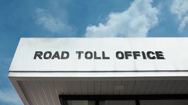 A Road Toll Office word sign displayed on a governmental or transport building under a clear blue sky, symbolizing road infrastructure, fee collection, public works, highway administration, and fiscal