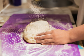 A hand dusting a portion of raw dough with a cloud of flour on a bright purple, showcasing the start of baking preparation.