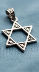 An intricate silver Star of David charm is captured in a detailed close-up. Lying on a soft blue background, this piece of jewelry represents a personal connection to faith and tradition.