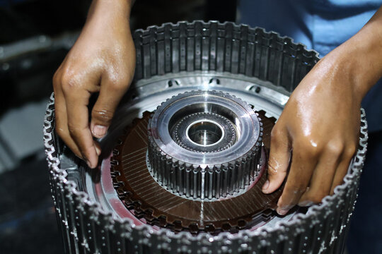 A technician's oily hands assembling a clutch friction plate onto the metallic hub of an automatic transmission clutch pack, detailing automotive repair work.
