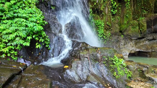  tropical paradise at Taman Sari Waterfall, where clear waters cascade into serene pond, inviting visitors to enjoy peaceful moments in jungle setting