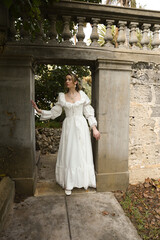 Fototapeta premium Full length female figure of beautiful blonde model wearing white fantasy wedding gown. walking through doorway of historical fairytale castle location 