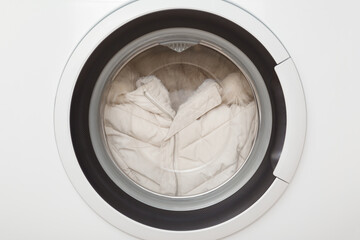 White warm female winter jacket with fur hood in closed washing machine. Delicate clothes care. Closeup. Front view.