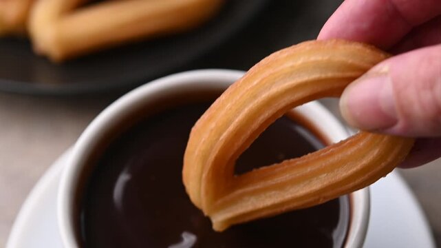 Hand dipping a churro in a cup of hot chocolate