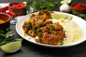 Delicious chicken tikka masala with rice, parsley and lime on dark textured table, closeup