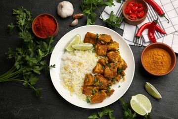Delicious chicken tikka masala with rice, parsley, lime and spices on dark textured table, flat lay