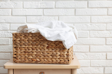 Wicker basket with laundry on table near white brick wall. Space for text
