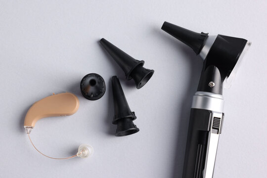 Modern otoscope, hearing aid and ear speculums on light grey background, flat lay - Powered by Adobe