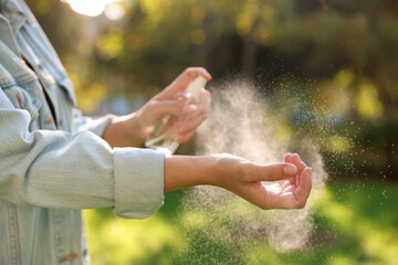 Woman spraying tick repellent onto hand in park, closeup