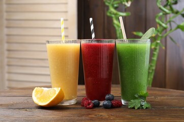 Different tasty smoothies in glasses and ingredients on wooden table, closeup