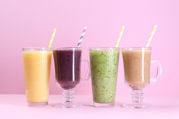 Different tasty smoothies in glasses on pink background