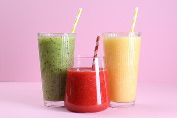 Different tasty smoothies in glasses on pink background