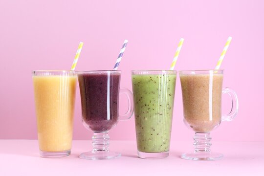 Different tasty smoothies in glasses on pink background