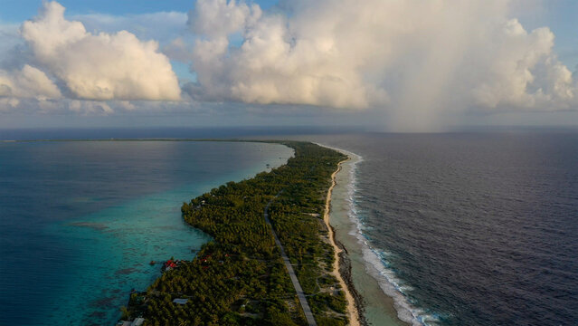 Aerial view of the slender landmass kissed by the turquoise lagoon on one side and the deep blue sea on the other, Rangiroa, Tuamotu Islands, French Polynesia.