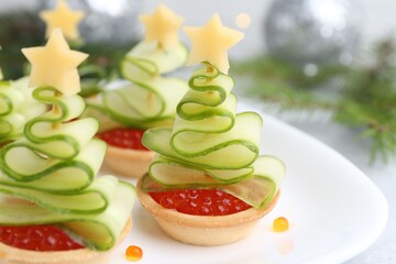 Christmas tree shaped tartlets made with red caviar, cucumber, cheese and festive decor on table, closeup