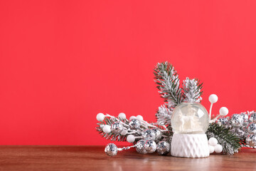 Fir tree branches, snow globe and other Christmas decor on wooden table against red background. Space for text