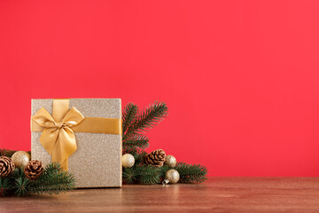 Fir tree branches, gift box and other Christmas decor on wooden table against red background. Space for text