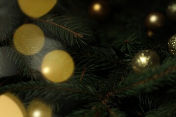 Beautiful spruce tree branches with Christmas ornaments and blurred lights as background, closeup. Bokeh effect