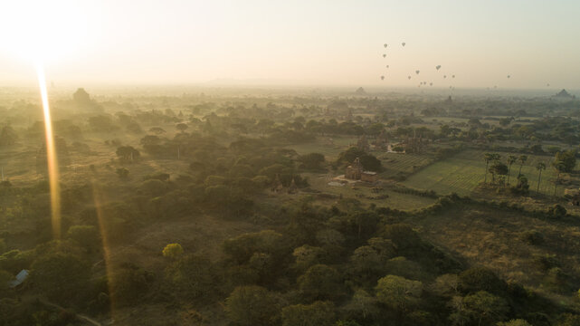 Aerial view of hot air balloons float serenely over ancient temples and lush landscapes bathed in the soft, golden light of dawn, Old Bagan, Mandalay Region, Myanmar.