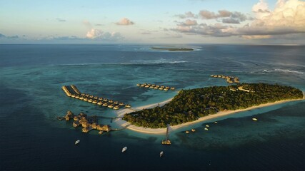 Aerial view of turquoise waters embrace the sandy shores of Filitheyo Island, where thatched-roof bungalows stand like jewels, Faafu Atoll, Maldives.