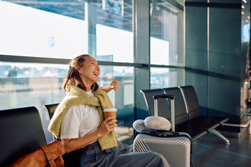 Asian woman laughing while drinking coffee, waiting for her airplane in a modern airport departure lounge with luggage