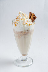 A tall glass filled with a creamy dessert, topped with whipped cream and caramel drizzle