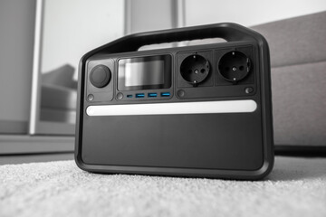 A modern portable power station sits indoors on a carpeted floor showcasing multiple outlets and USB ports for home or travel backup electricity needs.
