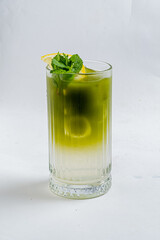 Chilled green beverage sits in a tall glass, garnished with fresh mint and a slice of lemon