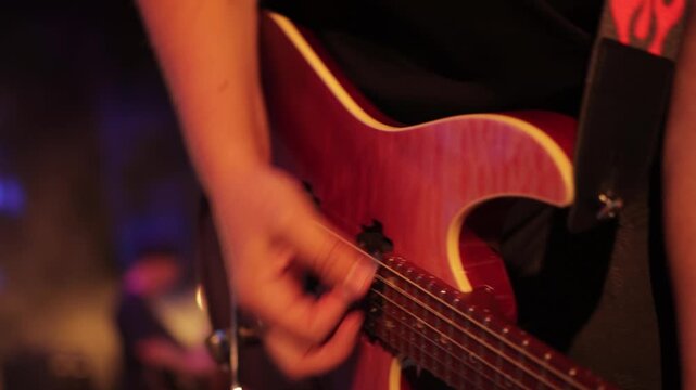 A man's hand playing the strings of an electric guitar, close-up