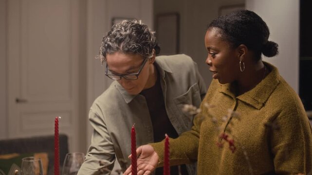 Medium long shot of four multiethnic friends setting table with snacks and baked food while gathering for Thanksgiving celebration at home