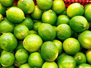 Fresh limes stacked in a red basket at a local market during a sunny day