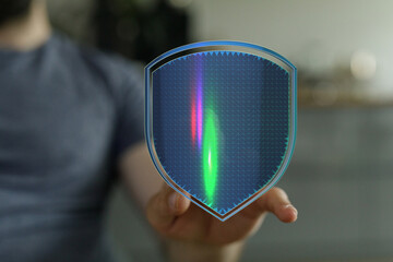 A person's hand holding a shield with a digital grid overlay, symbolizing security, data protection, and technological advancement. A