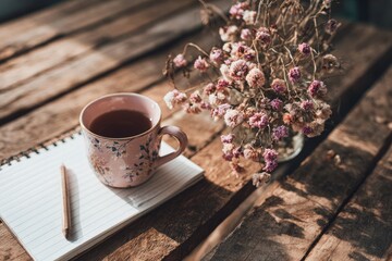 Pink Teacup On Wooden Table With Dried Flowers And Notebook