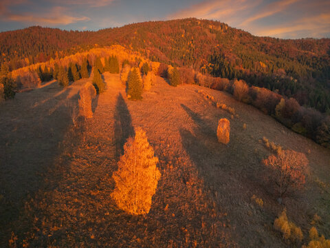 Aerial view of rolling hills bathed in the warm glow of sunset, casting long shadows across the landscape, Lubietova, Banska Bystrica Region, Slovakia.