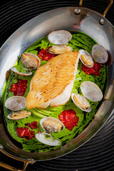 Freshly grilled fish rests on a vibrant green sauce, surrounded by clams and garnished beautifully