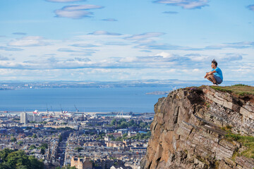 Tourist perched on cliff, taking in urban landscape and ocean