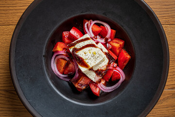 A vibrant salad features diced tomatoes and onion, topped with creamy cheese and tangy dressing