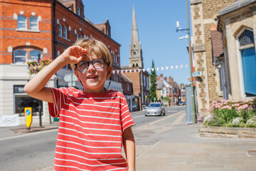 Happy boy shades eyes in sunny town street, red striped shirt