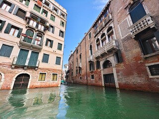 Narrow Venetian canal with red brick buildings and reflections on the water