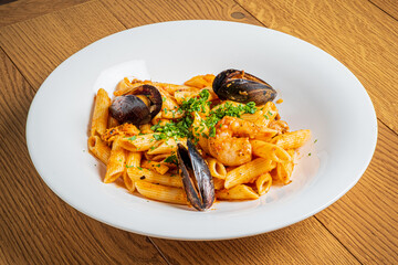 Tasty penne pasta topped with shrimp and mussels, garnished with fresh herbs on a wooden table