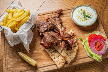 A hearty meal on a wooden platter with grilled meat, salad, creamy dip, and crispy fries