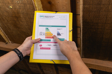Une personne en train de tenir le formulaire du DPE pour l'immobilier. Son autre main pointe vers...